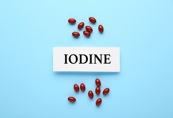 Card with word Iodine and pills on light blue background, flat lay