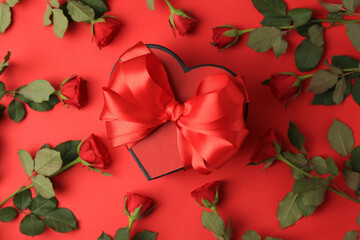 Heart shaped gift box with bow and beautiful roses on red background, flat lay