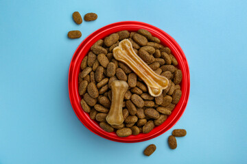 Dry dog food and treats (chew bones) on light blue background, flat lay
