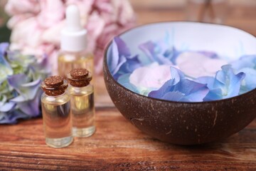 Obraz na płótnie Canvas Spa composition. Aromatic water in bowl, bottles of essential oil and flowers on wooden table, closeup