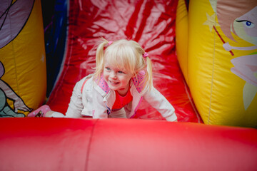 Fototapeta na wymiar a little girl 3 years old rolls down an inflatable bright slide, fun childhood, outdoor games