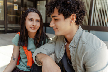 Tattooed young students sitting, indian girl looking lovingly at young man. Concept of relationships