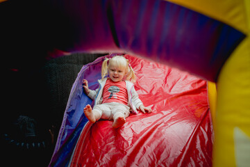 a little girl 3 years old rolls down an inflatable bright slide, fun childhood, outdoor games