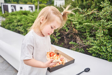 Cute happy girl cuts and eats in the park. Baked a delicious pizza Margarita in a traditional wood-burning oven in a Neapolitan restaurant, Italy. Pizza delivery concept in a cardboard box. 
