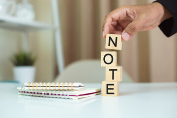 Word NOTE on wood cubes, Hand holding wooden block stacking with note alphabet and notebooks nearby on office table. inspiration creativity concept.