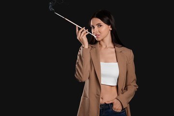 Fototapeta premium Woman using long cigarette holder for smoking on black background, space for text