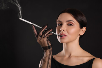 Woman using long cigarette holder for smoking on black background