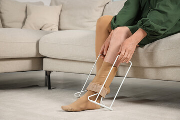 Woman putting on compression tights with stocking donner in living room, closeup. Prevention of...