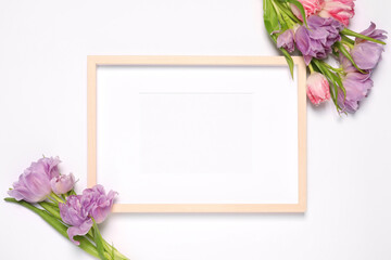 Empty photo frame and beautiful tulip flowers on white background, flat lay. Mockup for design