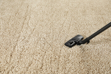 Hoovering beige carpet with modern vacuum cleaner. Space for text