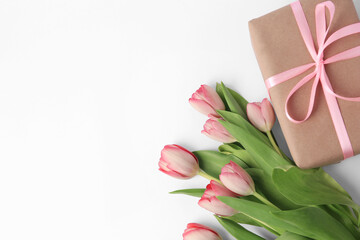 Beautiful gift box with bow and pink tulips on white background, flat lay. Space for text