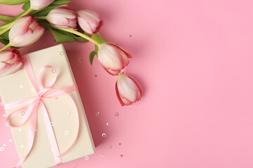 Beautiful gift box with bow, tulips and confetti on pink background, flat lay. Space for text
