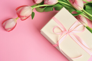 Beautiful gift box with bow and tulips on pink background, above view. Space for text