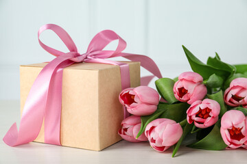 Beautiful gift box with bow and pink tulip flowers on white table, closeup