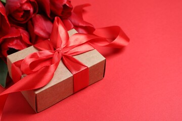 Beautiful gift box with bow and tulip flowers on red background, closeup. Space for text