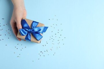 Woman with gift box and confetti on light blue background, top view. Space for text