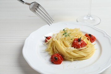Eating tasty capellini with tomatoes and cheese at white wooden table, closeup. Exquisite presentation of pasta dish