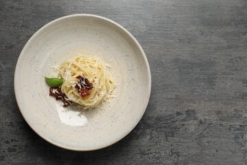 Tasty spaghetti with sun-dried tomatoes and cheese on grey table, top view and space for text. Exquisite presentation of pasta dish
