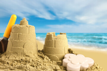 Sand castles with toys on ocean beach, closeup. Outdoor play