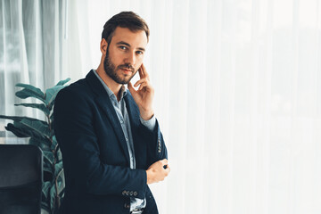 Handsome businessman in black suit stand confidently in his modern office portrait, deep in thought...