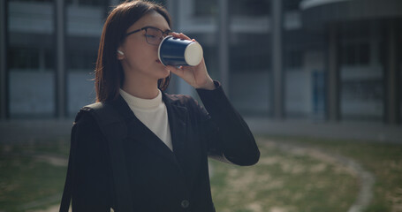 Young business woman in formal suit holding paper coffee cup sipping coffee to relax at outdoor