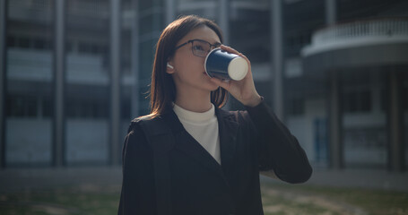 Fototapeta premium Young business woman in formal suit holding paper coffee cup sipping coffee to relax at outdoor