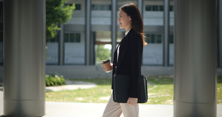 Charming Young Asian businesswoman in suit holding a cup of coffee and walking