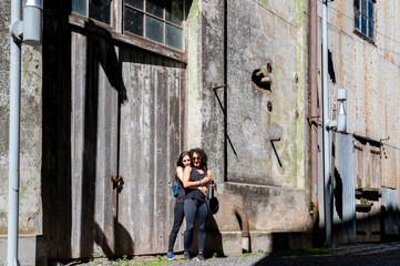 Women smiling and hugging while posing outside an abandoned factory.