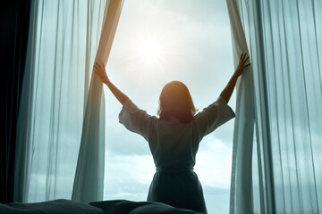 In the morning, a woman opens the curtains of the window in the bedroom. woman stretching at the...