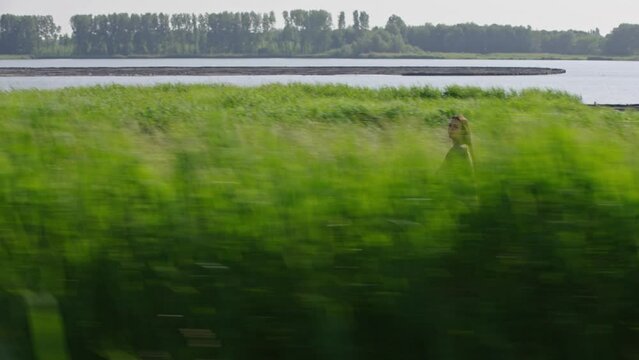 Lady cycles on pathway through lush vegetation on river bank, parallel tracking