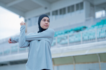 A young asian Muslim woman wearing a black hijab is exercising and running at an outdoor stadium in the morning. Modern Muslim woman concept,  Muslim woman sport concept, Islam