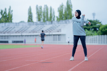 A young asian Muslim woman wearing a black hijab is exercising and running at an outdoor stadium in the morning. Modern Muslim woman concept,  Muslim woman sport concept, Islam