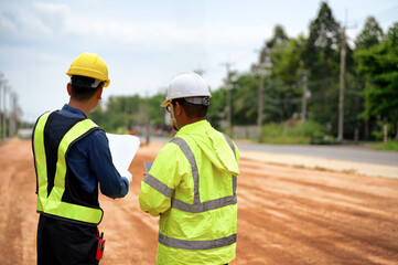 Asian Civil engineers consider and discuss with construction foremen while looking at blueprint...