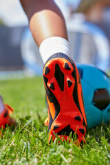 Close-up of a girl's foot with soccer boots on the soccer field. Blue ball and leg of a girl with...