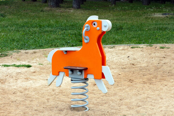 Swing rocking chair in the shape of an orange horse on the playground.
