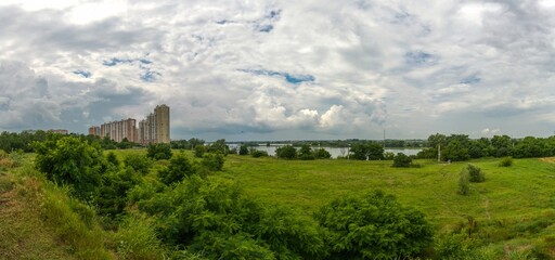 Fototapeta na wymiar panorama of the coast of the Kuban river on the korai of the city of Krasnodar with a Polish wasteland and multi-storey buildings on a rainy summer day with thunderclouds