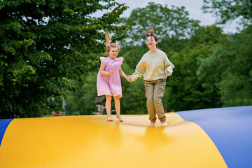 Little preschool girl and school sister jumping on trampoline. Happy funny children, siblings in...