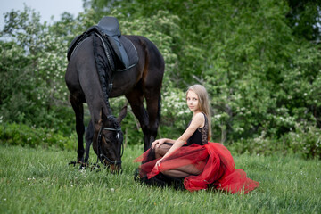 a girl in a beautiful dress sits on the green grass next to the horse