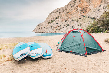 Camping tent with sup boards on the wild beach at mediterranean seacoast. Water trip and sportive recreation © EdNurg