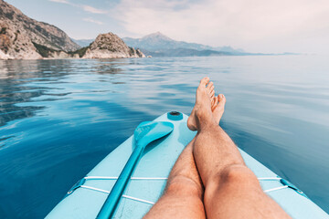 Men's legs and paddle on a supboard against the backdrop of a picturesque seascape with a rocks....