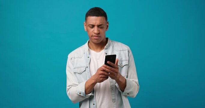 Young african american man using mobile cell phone typing when looking at camera surprised and disappointed