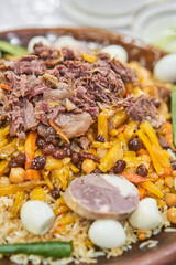 A traditional Uzbek dish called pilaf. Rice with meat, carrots, onions, quail eggs and kazy in a plate of astau on the table. A portion for three people.
