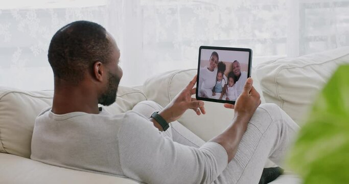 Young and happy african man sitting on sofa in living room at home use tablet making video call for funny talking to his friend or sibling family while city lockdown. Social distancing concept.