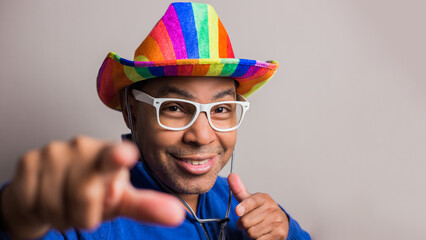 young dark-haired man with lgbt flag hat and white glasses