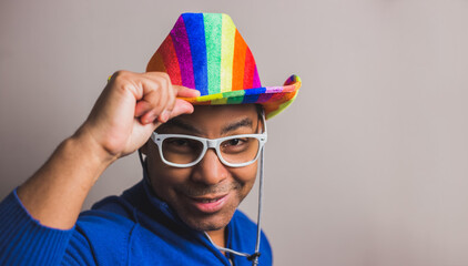 young dark-haired man with lgbt flag hat and white glasses