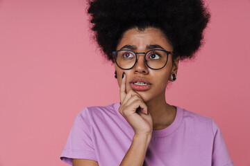 Pensive afro woman touching her chin while standing isolated over pink wall