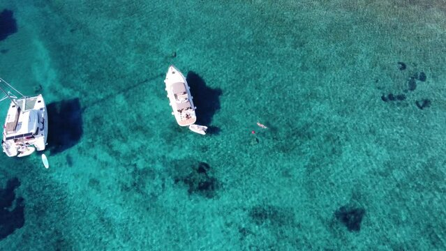 Woman on a boat trip swimming in turquoise clear water of blue lagoon in Croatia beside anchored Catamaran yacht. Aerial