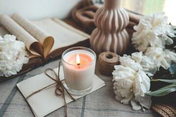 Fototapeta na wymiar Burning candle and white peonies, vintage aesthetic