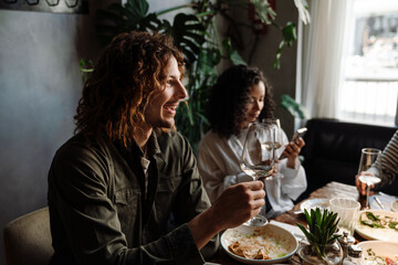 Cheerful man talking with friends and drinking wine while dining in restaurant