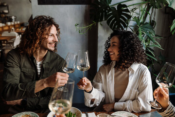 Group of smiling friends clinking wine glasses while dining in restaurant